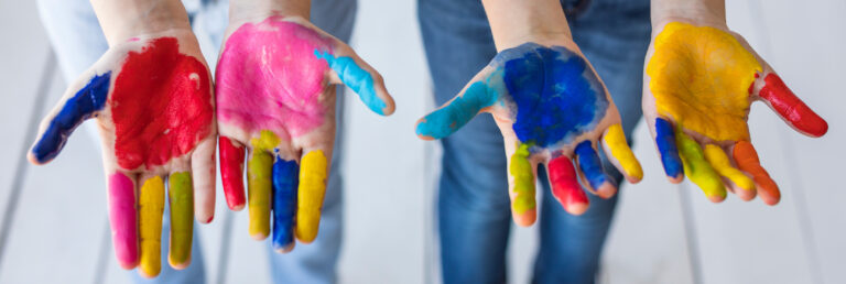 Foto van vier kinderhanden met verschillende kleuren verf op de handen.